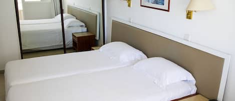A hotel room with two single beds, a wooden nightstand with a phone, and wall-mounted lamps.