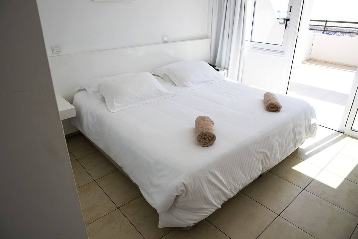 Habitación de hotel con una cama grande, ropa de cama blanca y dos toallas enrolladas sobre la cama.