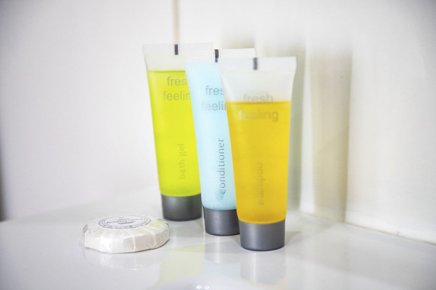 Três frascos de gel de banho e uma barra de sabonete em uma superfície branca.