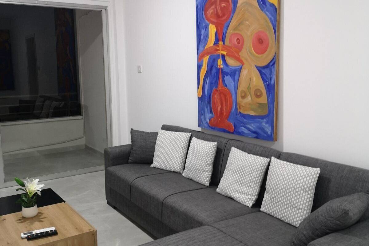 Una sala moderna con un sofá seccional gris, una mesa de centro de madera y un cuadro abstracto grande en la pared.