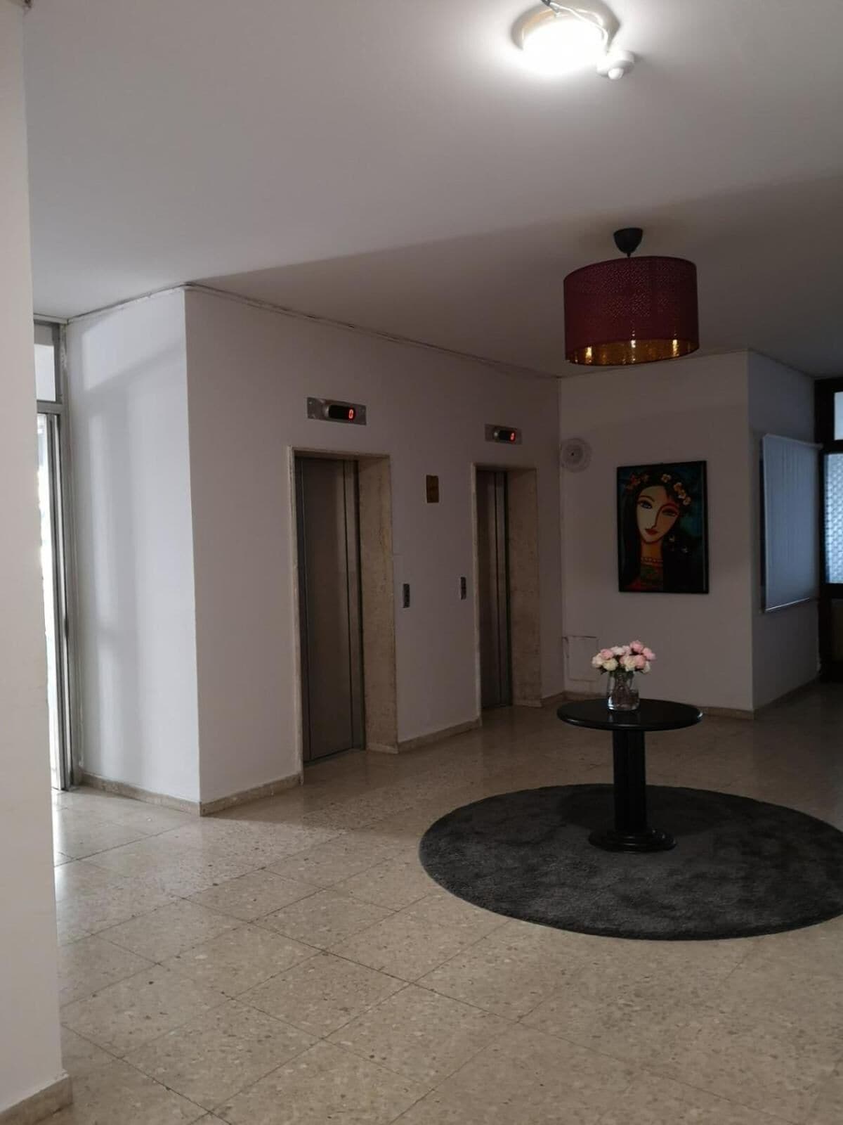 Un couloir avec deux ascenseurs, une table ronde ornée d’un vase de fleurs et un tableau accroché au mur.