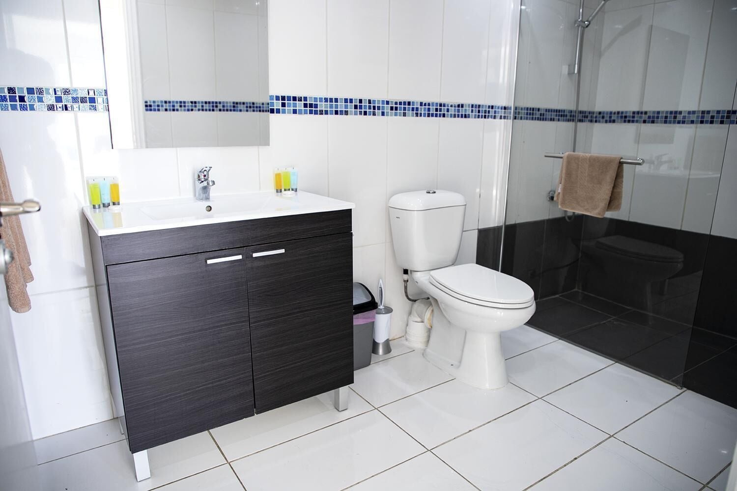 A modern bathroom with a white sink, dark cabinet, toilet, and a glass shower enclosure.