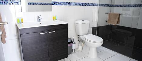 A modern bathroom with a white sink, dark cabinet, toilet, and a glass shower enclosure.