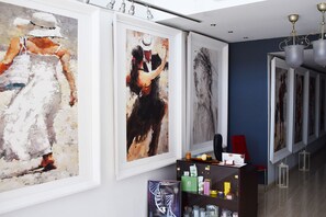 Um corredor com grandes pinturas abstratas nas paredes, uma receção com diversos objetos e um candeeiro moderno.