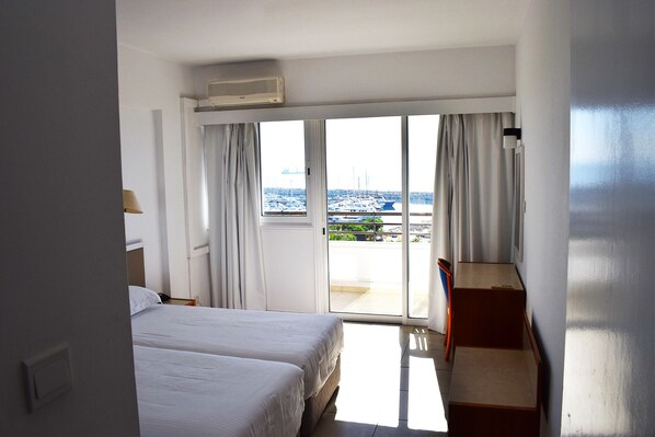 Quarto de hotel com duas camas, uma escrivaninha e vista para barcos através de uma janela grande.