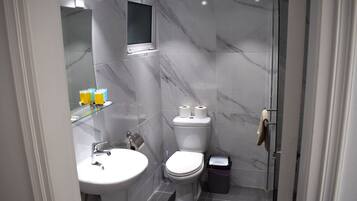A modern bathroom with a marble floor, a white sink, a toilet, and a glass shower enclosure.