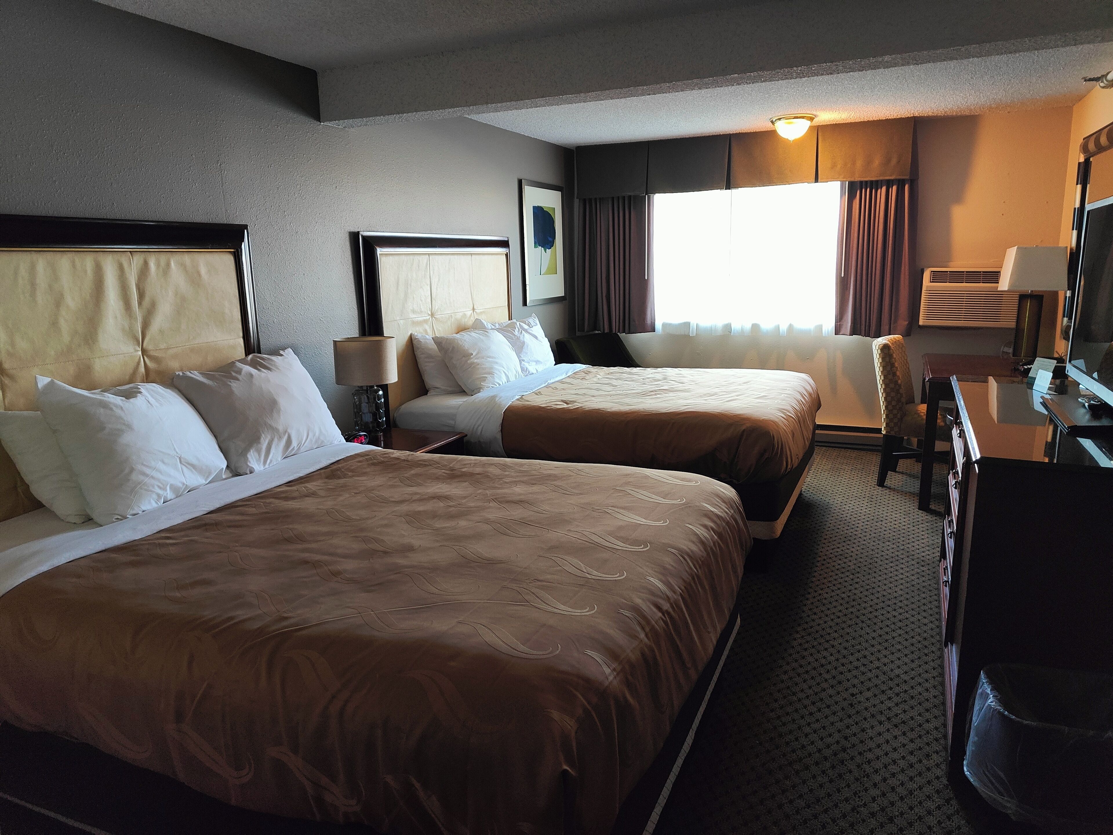 A hotel room with two beds, a desk, a chair, a TV, and a window with curtains.