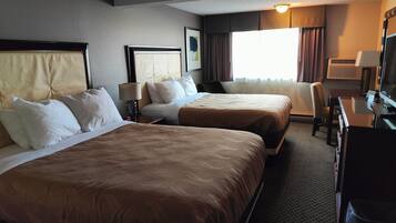 A hotel room with two beds, a desk, a chair, a TV, and a window with curtains.