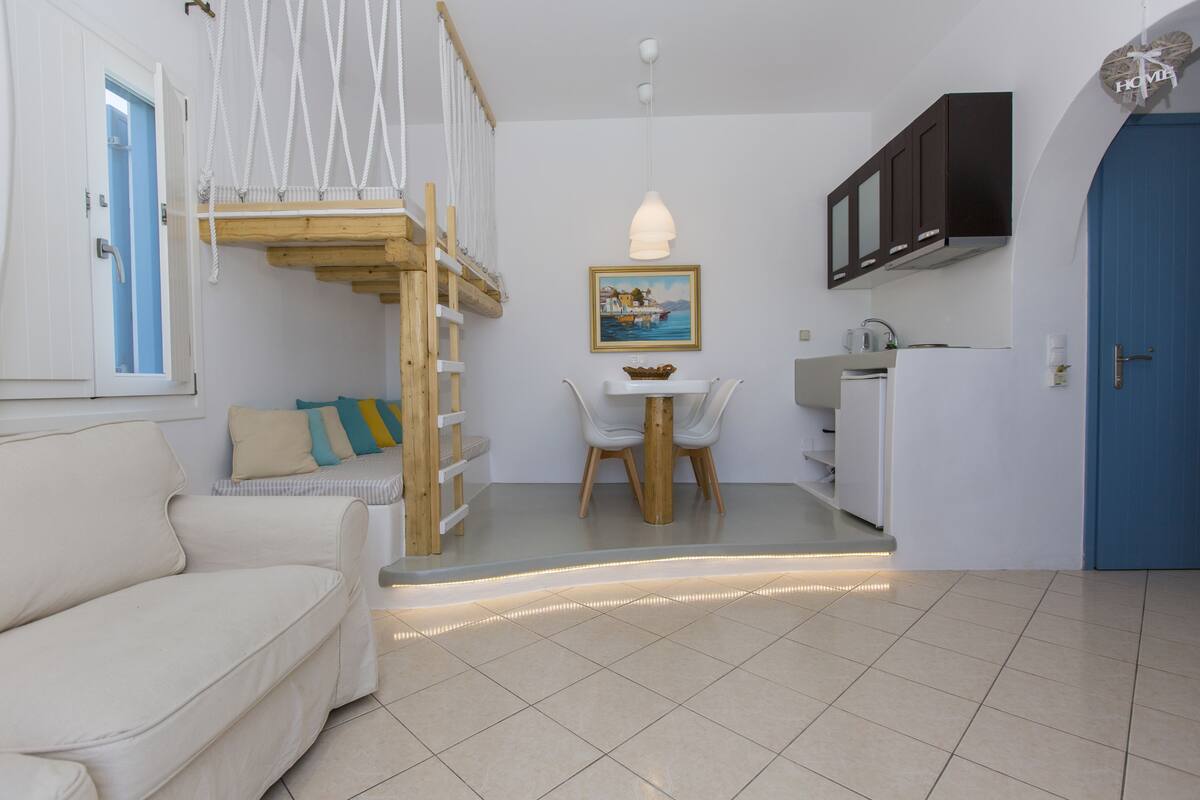 Um espaço compacto com sofá, mesa de jantar com cadeiras, cozinha e uma porta azul.