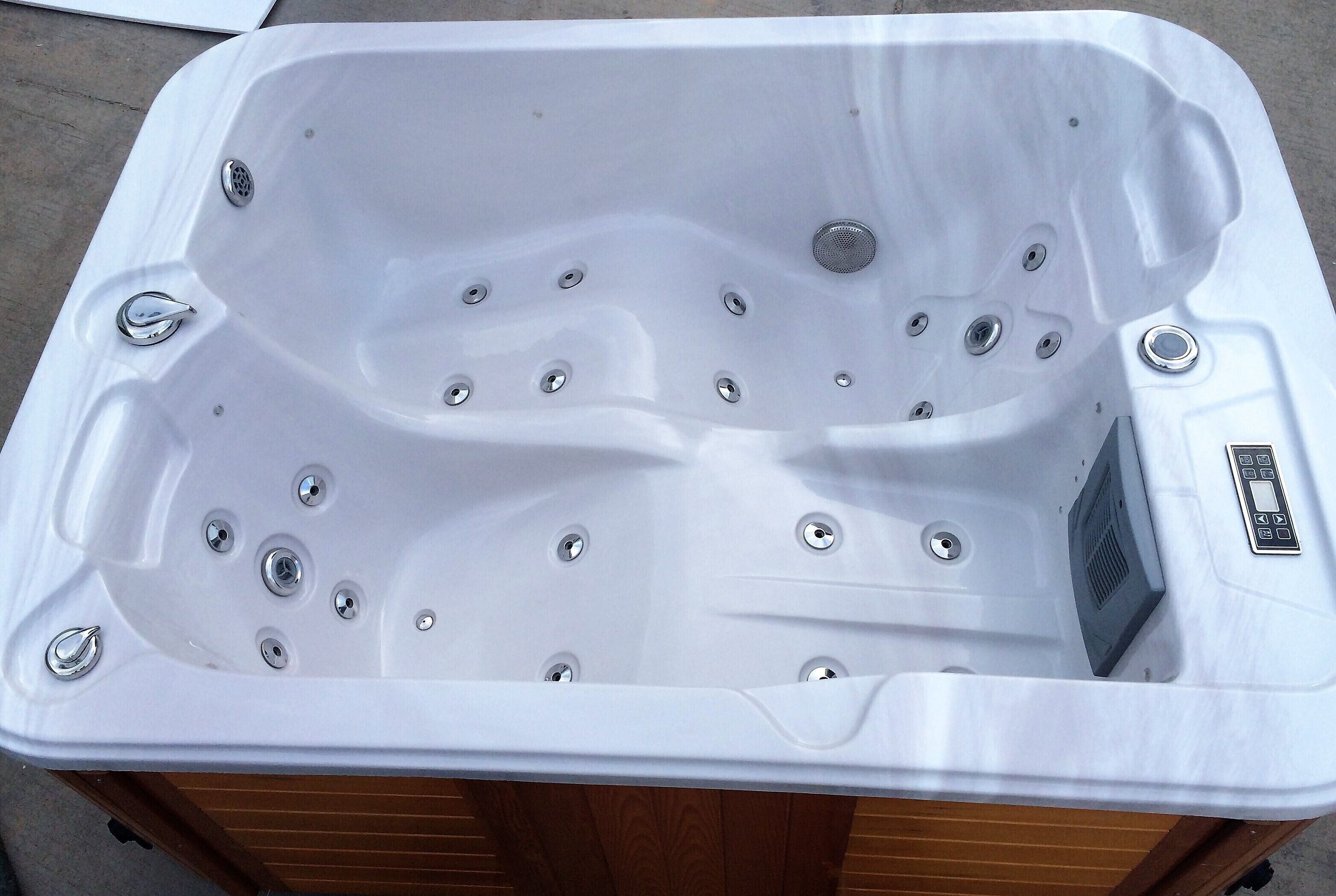 A white hot tub with multiple jets, a control panel, and a wooden base.