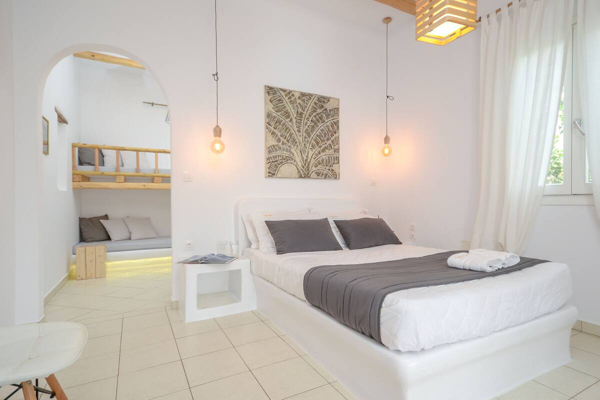 Quarto moderno com uma cama grande, mesas de cabeceira, um pequeno espaço de estar e vista através de um arco.