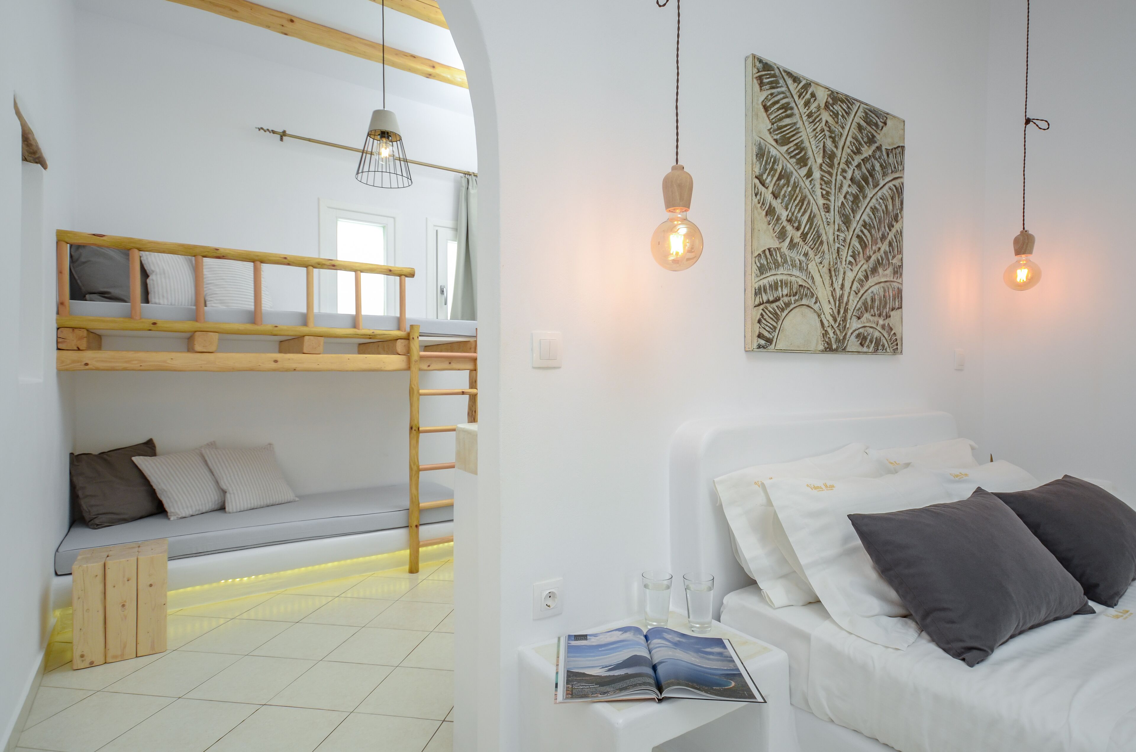 Una habitación con una cama litera, una mesita de noche con un libro y dos bombillas colgantes.