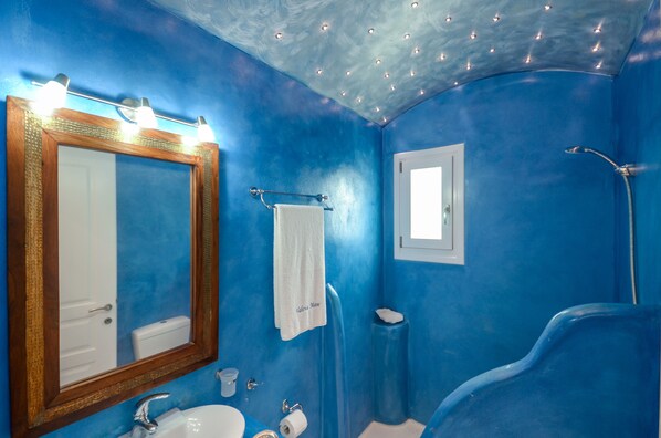A bathroom with blue walls, a wooden-framed mirror, a white sink, and a shower area. - Valena Mare (Naxos)