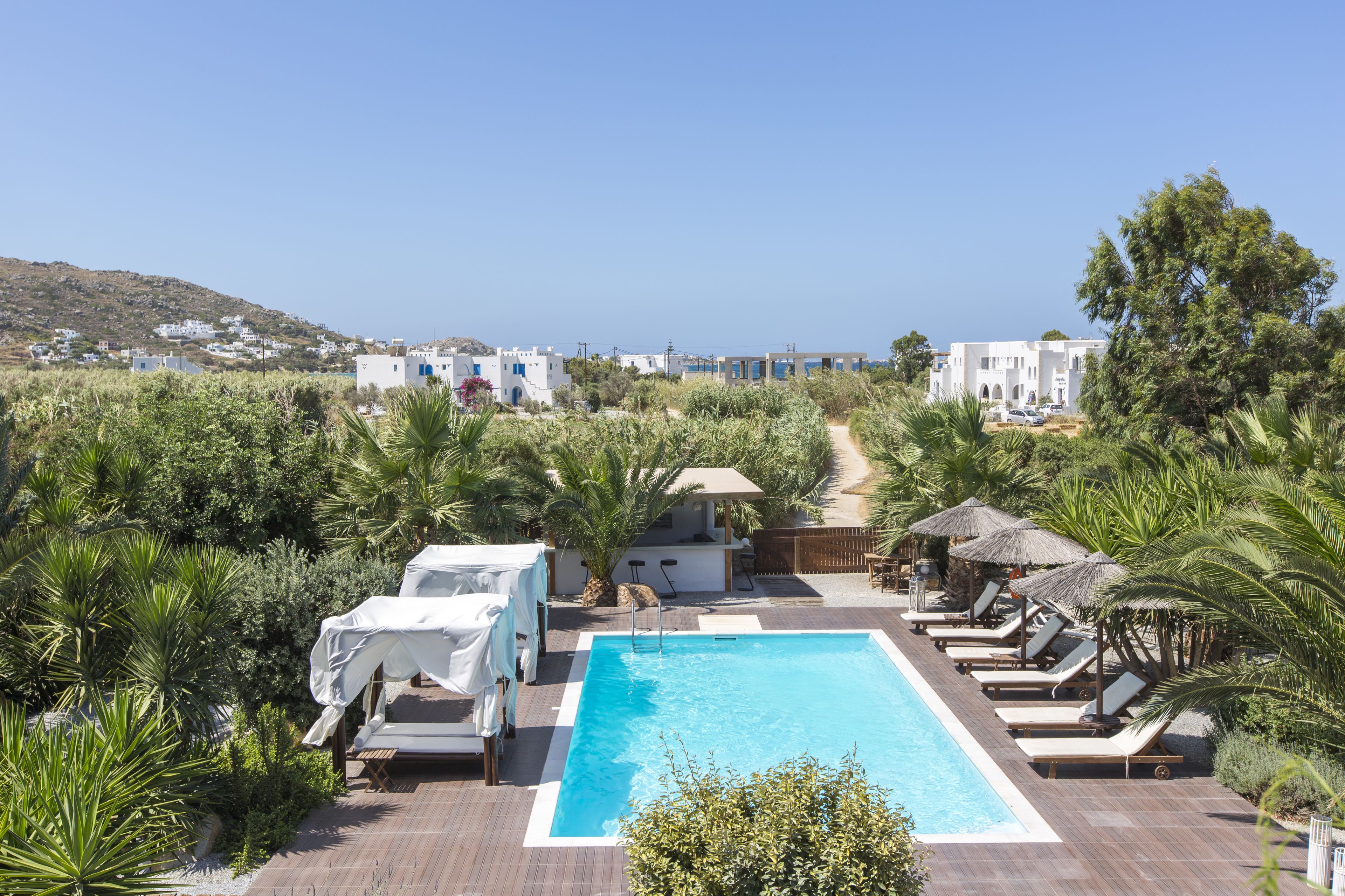 Une piscine rectangulaire, dotée de chaises longues et de parasols, entourée de verdure et offrant une vue sur un village côtier.