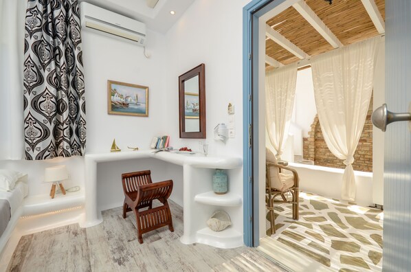 A room with a white and blue color scheme, featuring a wooden chair, a small table, a white shelf, and a window with white curtains. - Valena Mare (Naxos)