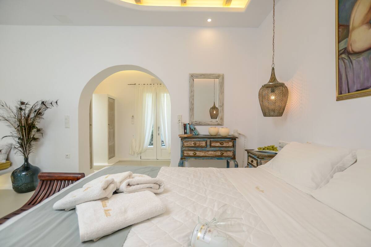Quarto com cama, mesa de cabeceira com vaso, cômoda e espelho.