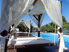 A poolside area with wooden loungers, white canopies, and a clear blue pool. - Valena Mare (Naxos)