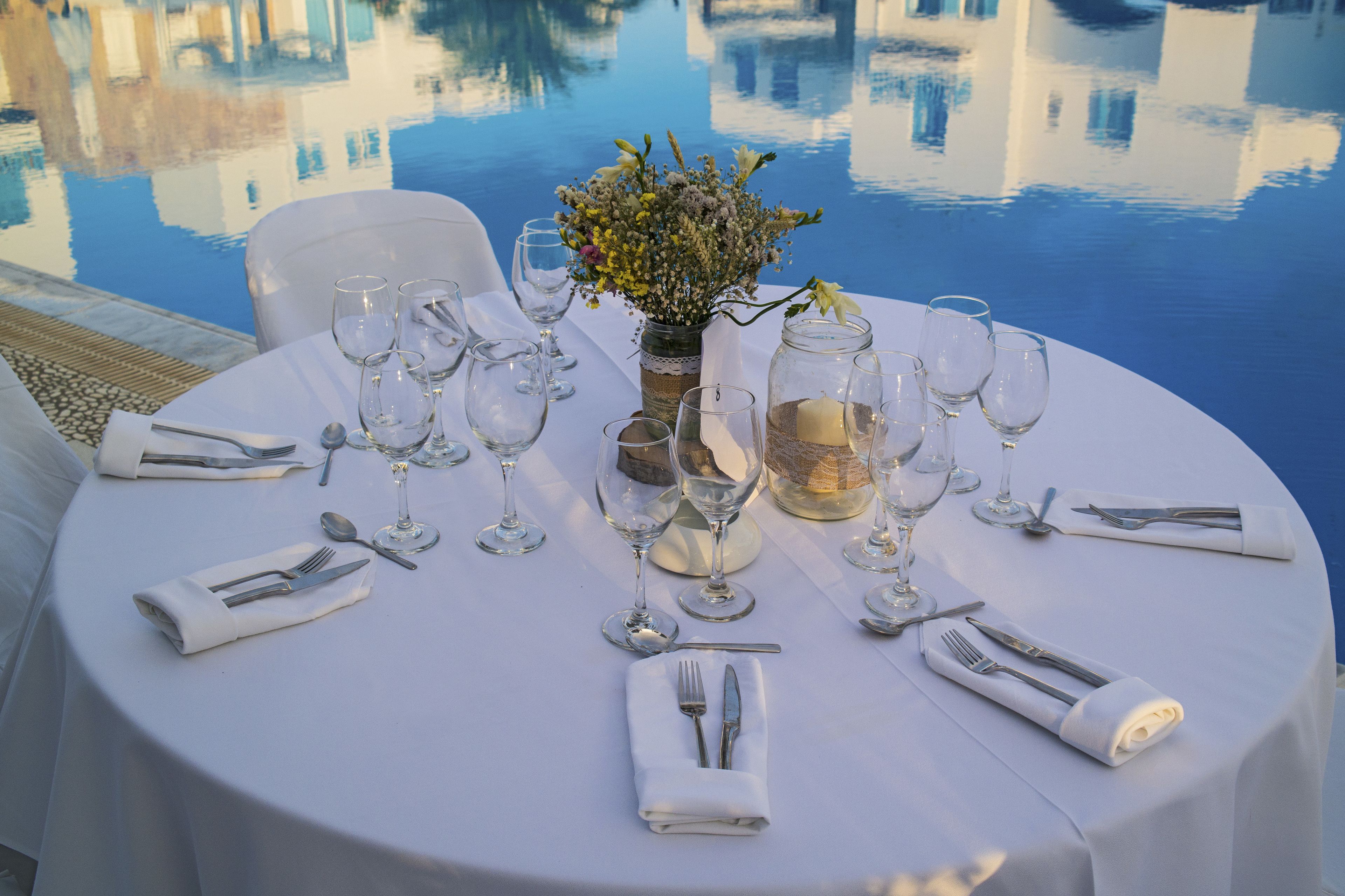 A round dining table set for six with white tablecloth, glassware, and silverware.