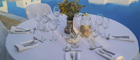 A round dining table set for six with white tablecloth, glassware, and silverware.