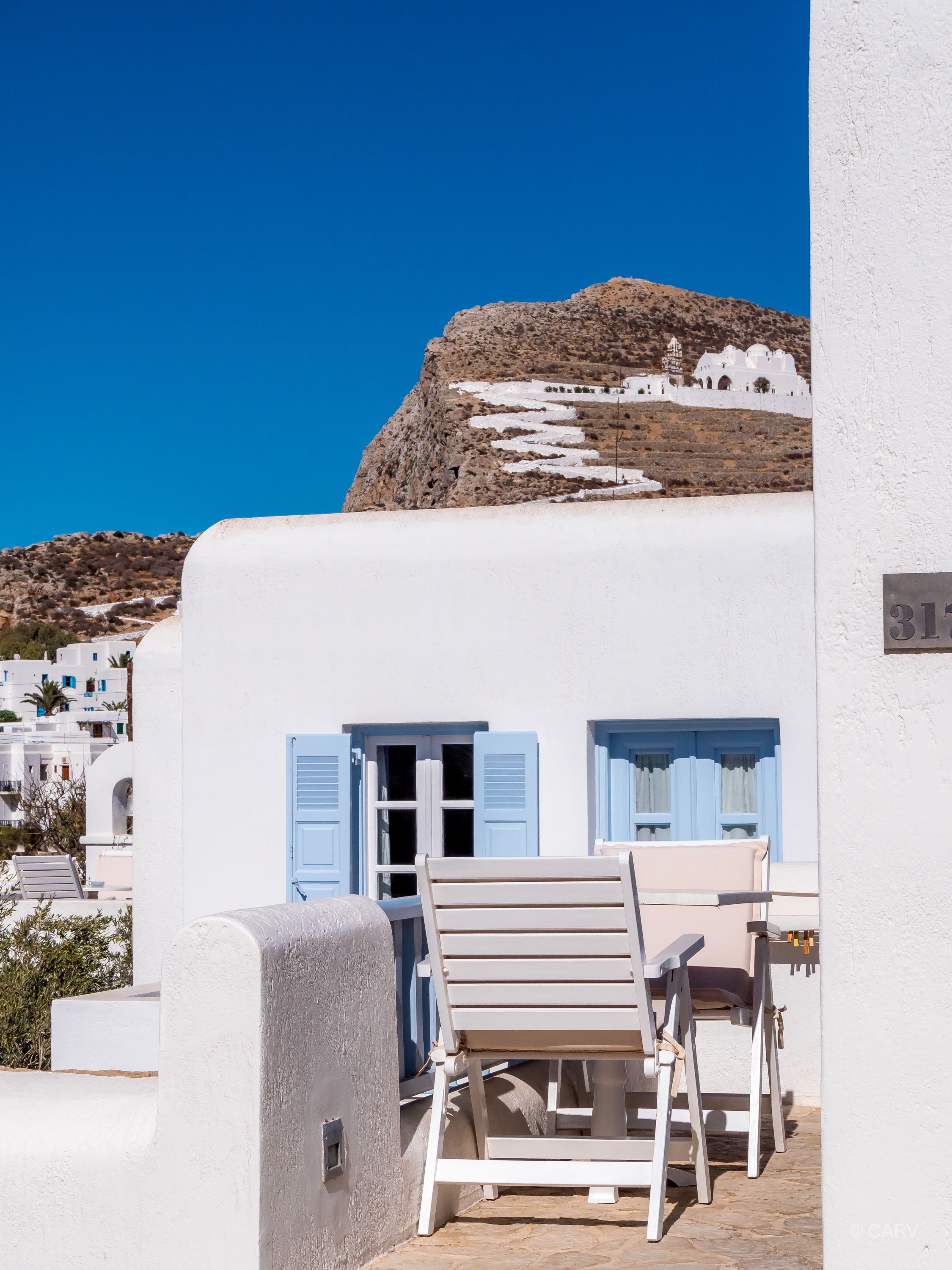 Un edificio bianco con persiane blu e un muro in pietra.