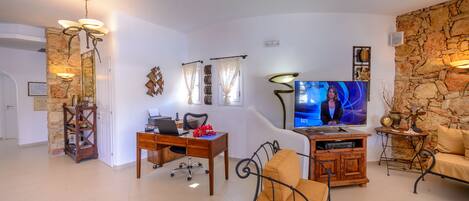 A living room with a stone wall, a TV, a desk with a laptop, a sofa, and a coffee table.