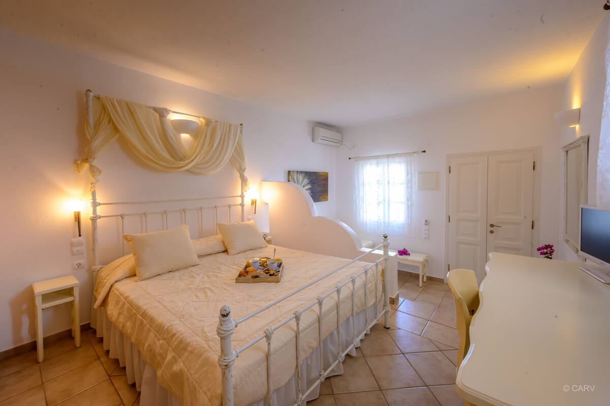 A bedroom with a bed, bedside tables, a desk, and a television.