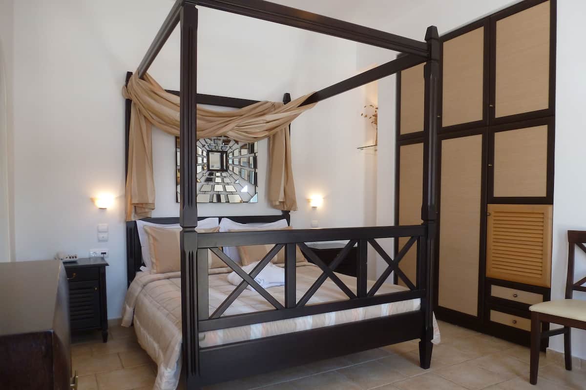 A four-poster bed with a canopy, a bedside table, a chair, and a decorative mirror on the wall.