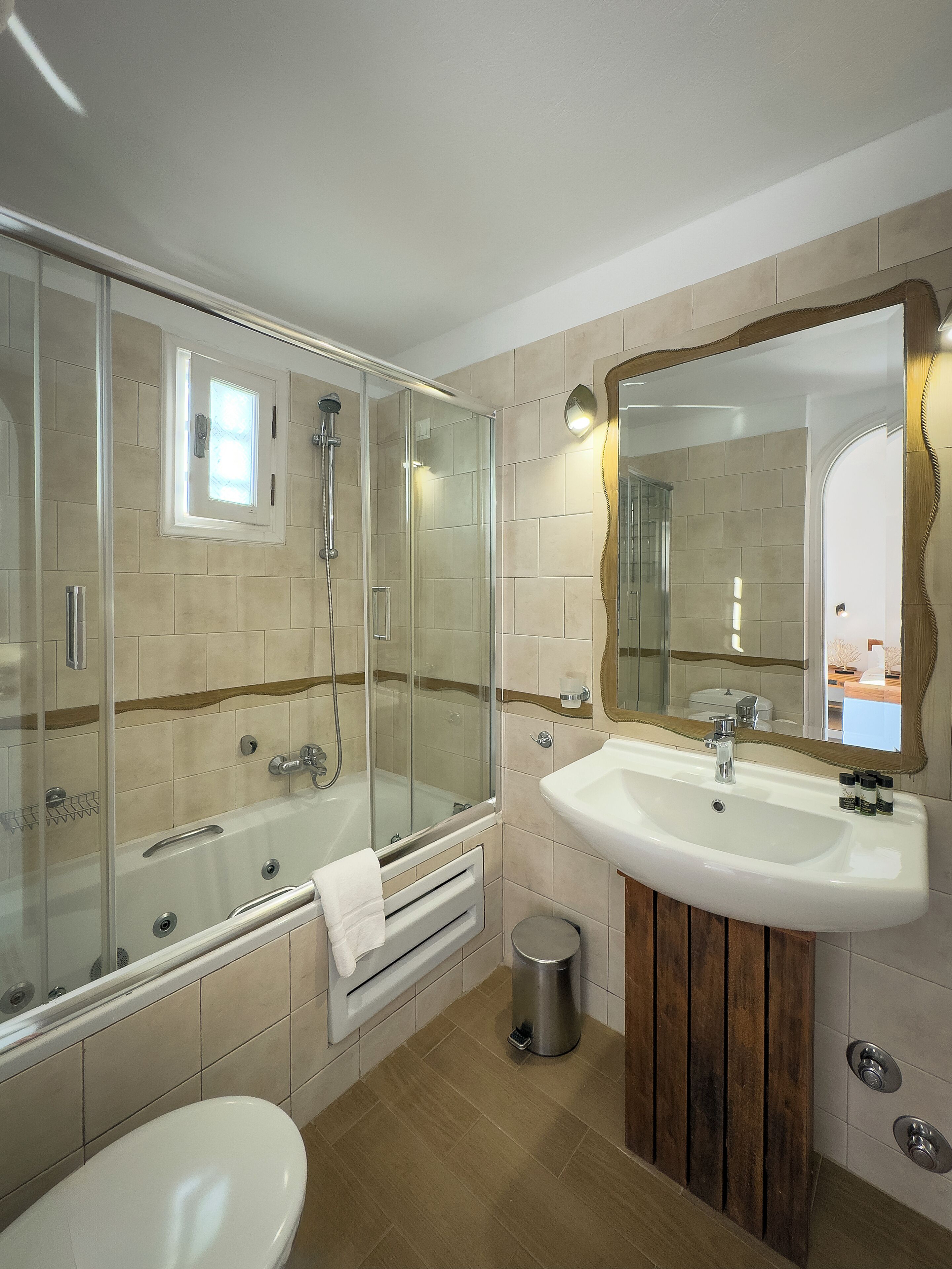 Un baño moderno con ducha envuelta en cristal, una bañera independiente, un lavabo con espejo y un inodoro.