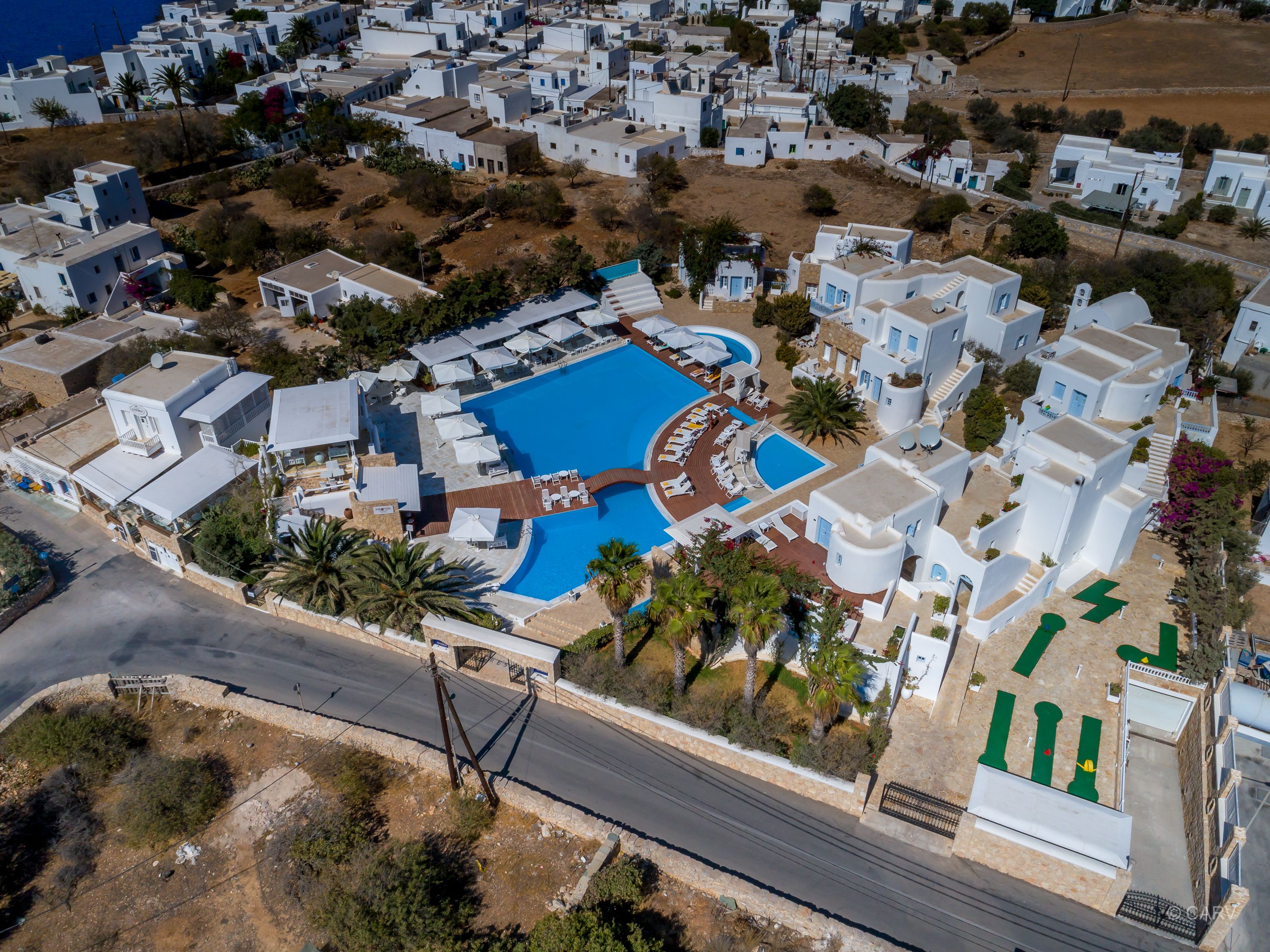 Oversigtsbillede af en kystferie med hvide bygninger, en central swimmingpool og palmer.