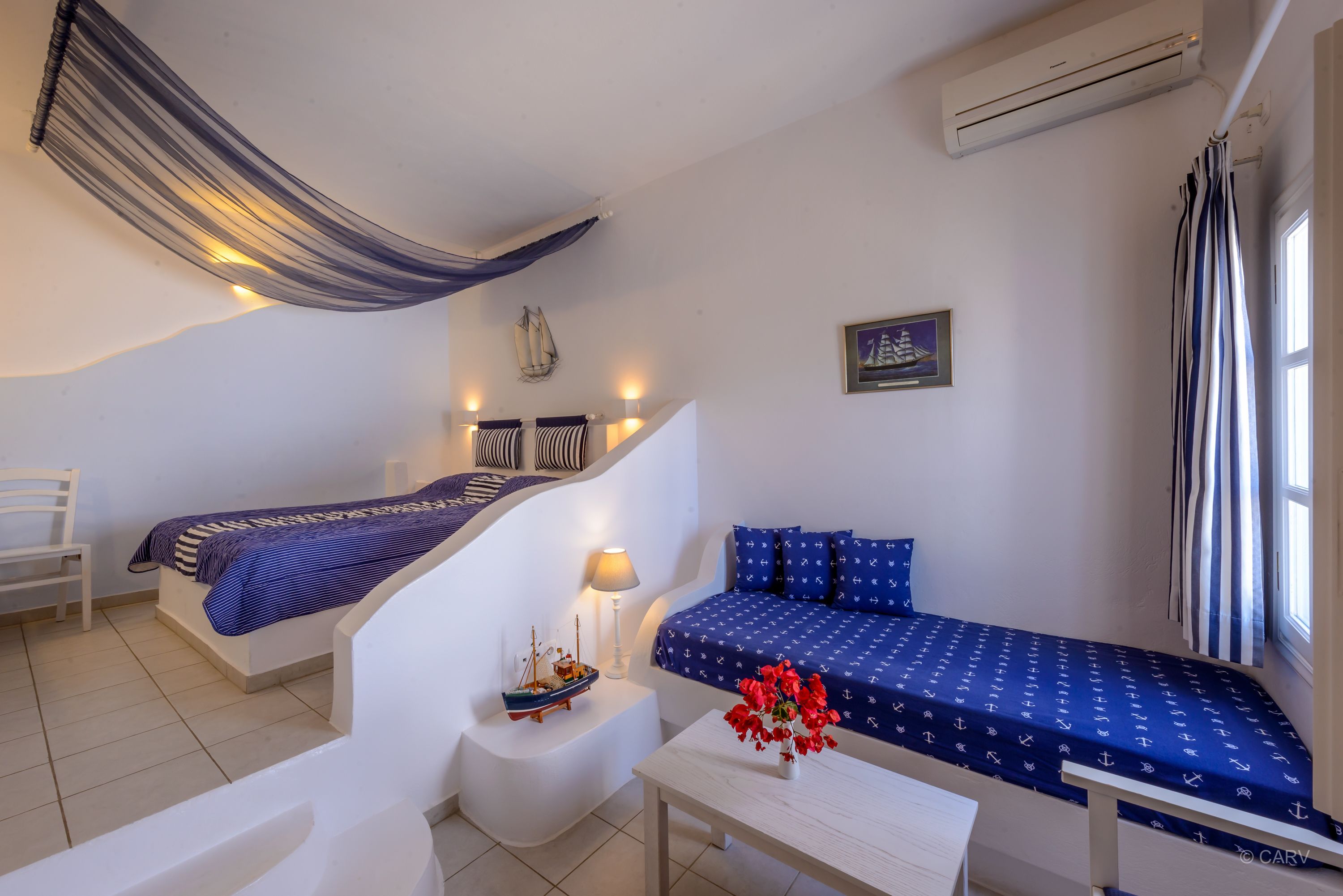 A compact room with two beds, a small table, a chair, and a hammock.