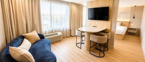 Une chambre d’hôtel moderne équipée d’un canapé, d’une table à manger avec des chaises, d’un téléviseur à écran plat et d’un lit.
