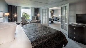 A hotel room with a large bed, two armchairs, a desk, and a television. - Hôtel Château Joliette (Joliette)