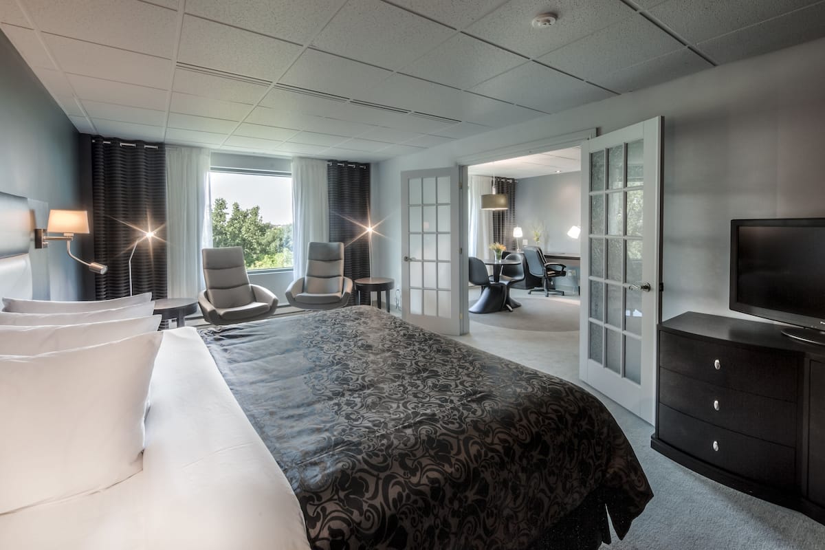 A hotel room with a large bed, two armchairs, a desk, and a television.