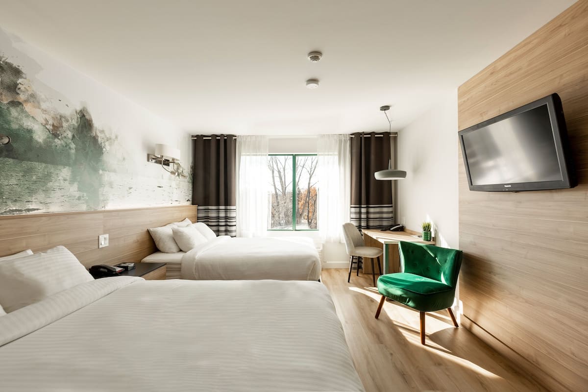 A hotel room with two beds, a desk, a chair, a TV, and a window with curtains.