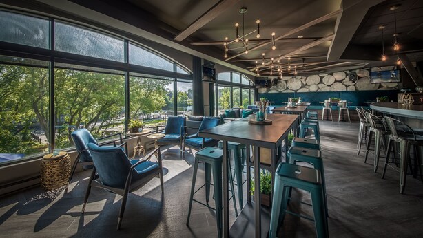 A modern restaurant with large windows, blue seating, and a stone wall. - Hôtel Château Joliette (Joliette)