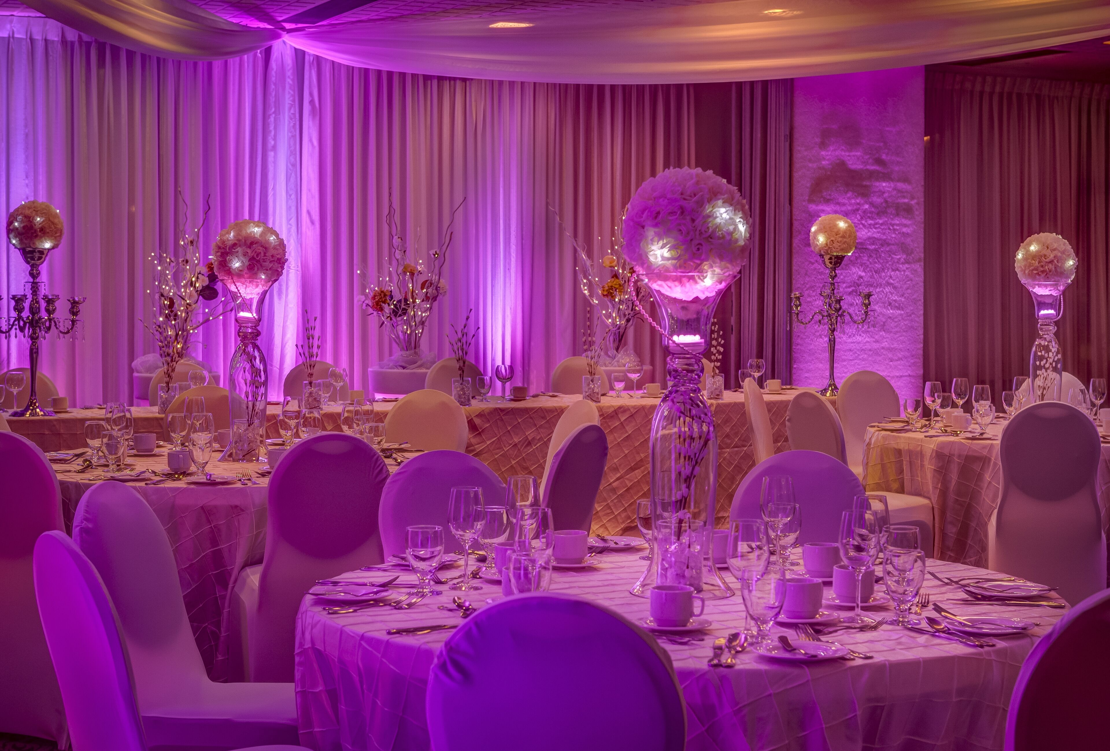 A banquet hall with round tables set for a formal event, featuring crystal chandeliers and floral centerpieces.
