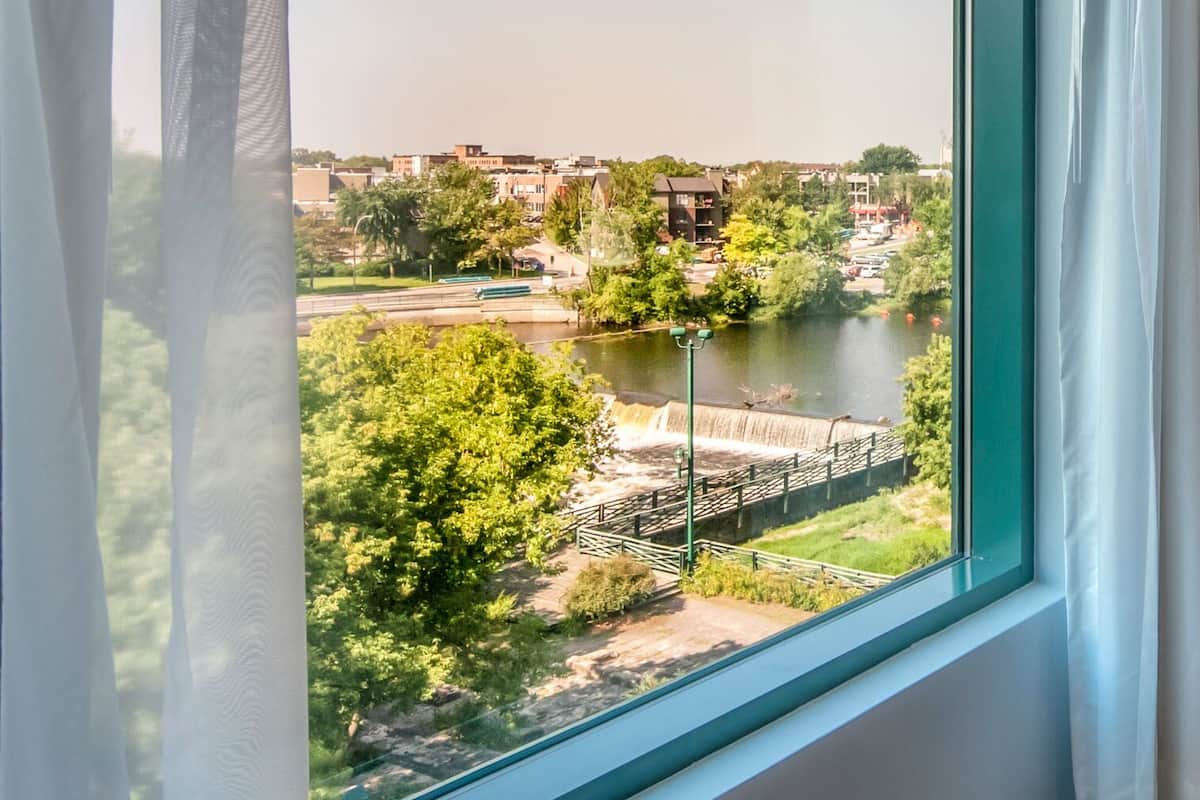 A view through a window with a clear view of a river, a bridge, and surrounding greenery.