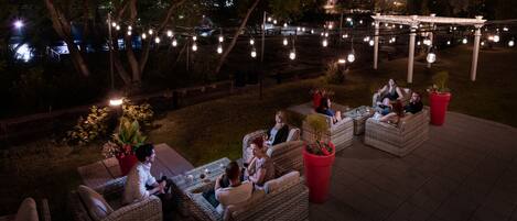 An outdoor seating area with wicker furniture and potted plants, under string lights.