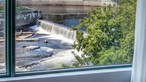 A view of a waterfall through a window, with a concrete structure and greenery in the background. - Hôtel Château Joliette (Joliette)