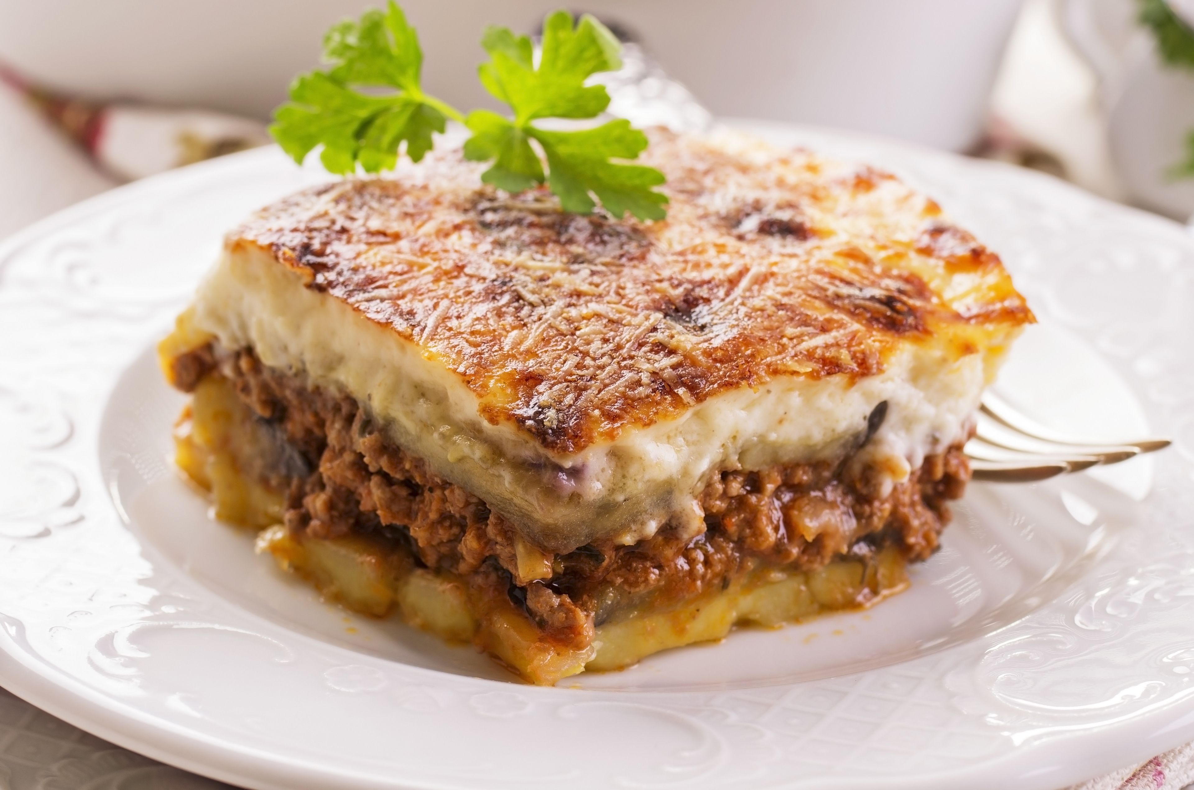 Una porción de lasaña en un plato blanco, adornada con perejil.