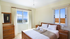 Un dormitori amb un llit, fallegueres, un prestatge de fusta, una finestra amb cortines i vista a l'oceà.