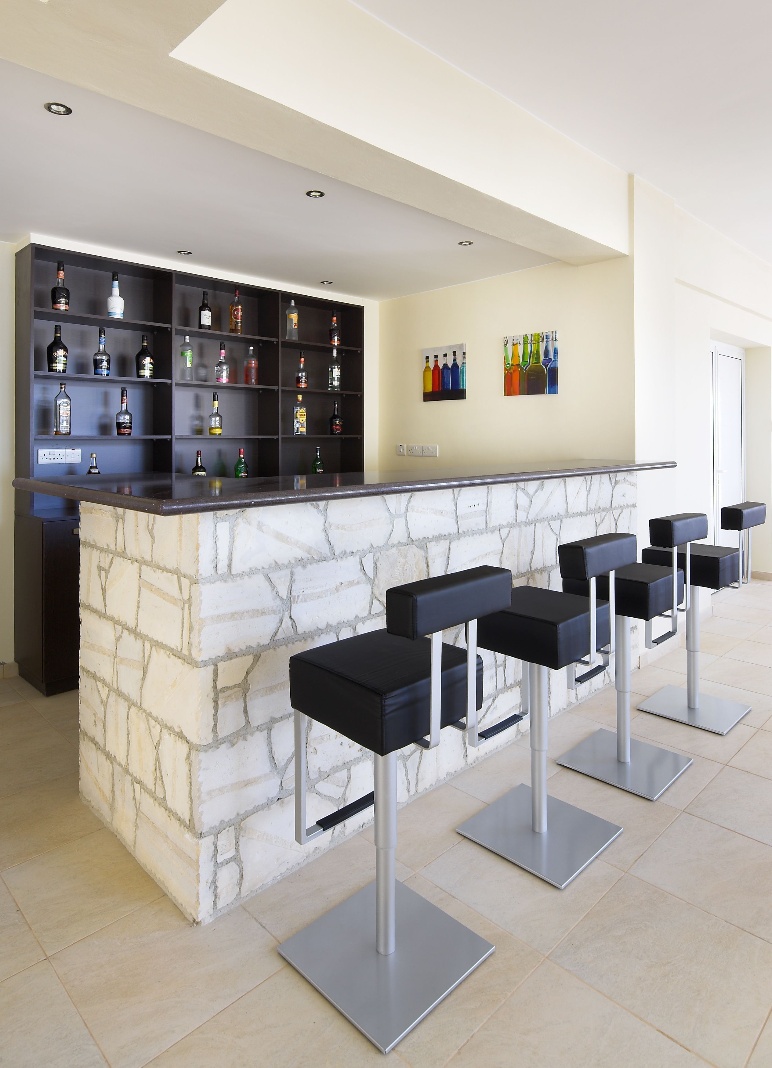 A bar area with a marble counter, black bar stools, and shelves of liquor bottles.