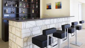A bar area with a marble counter, black bar stools, and shelves of liquor bottles.