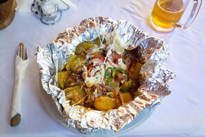 A meal in a foil bowl with a fork beside it, and a mug of beer in the background.