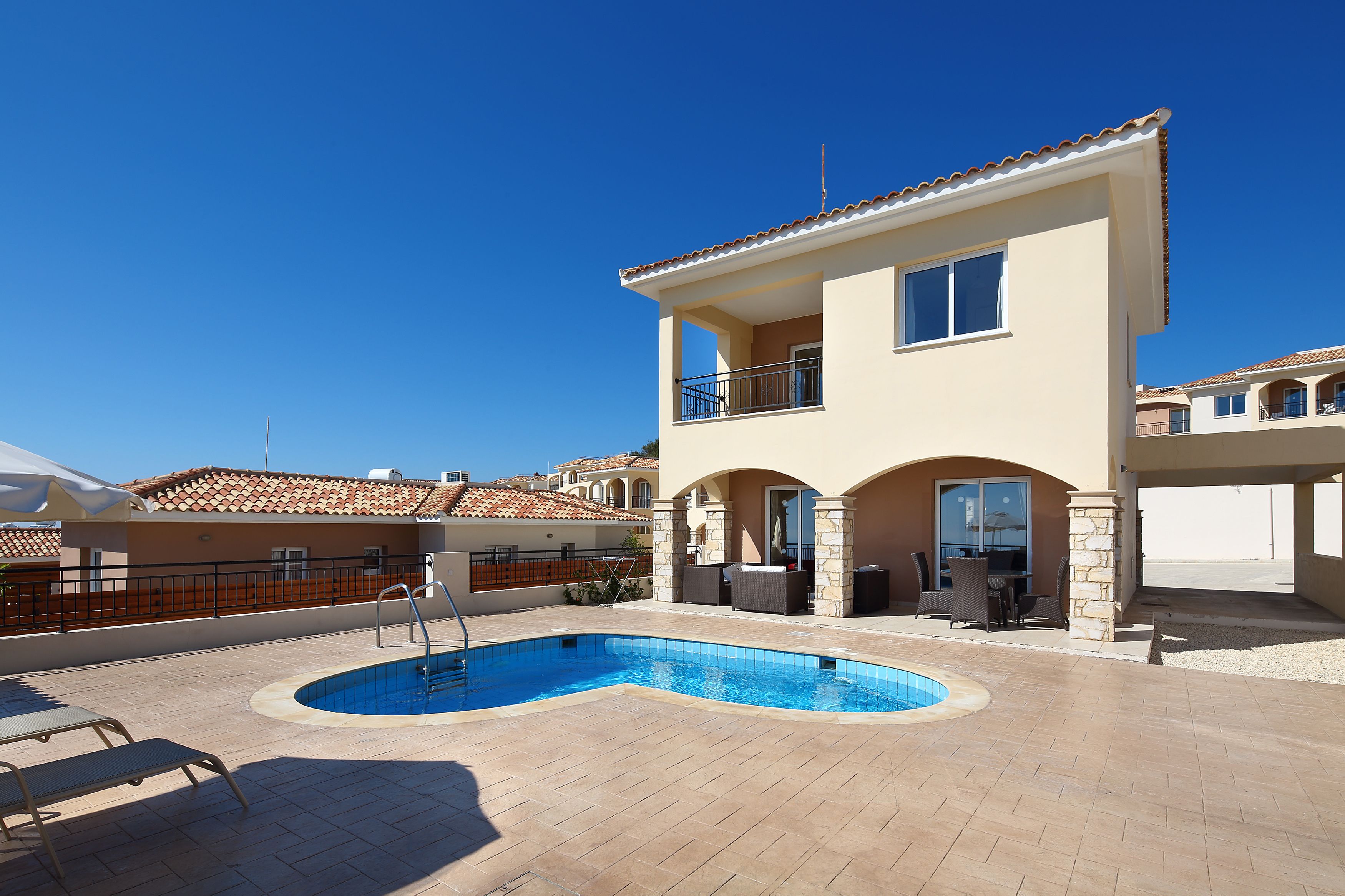 A two-story house with a swimming pool, outdoor furniture, and a clear blue sky.