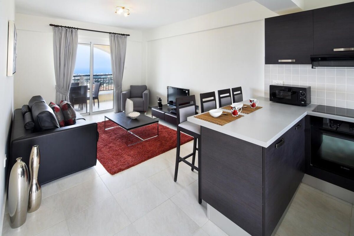 A modern kitchen with a central island, a dining area with a red rug, and a seating area with a sofa and chairs.
