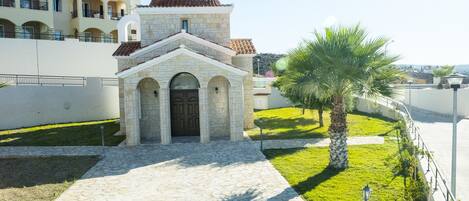 A stone church with a dome and arched entrance, surrounded by a well-maintained lawn and a palm tree.