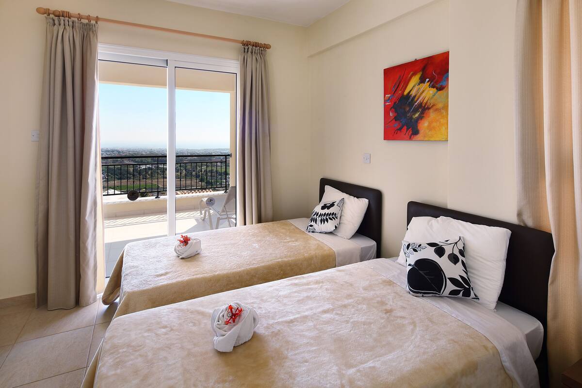A hotel room with two beds, a balcony with a view, and a painting on the wall.