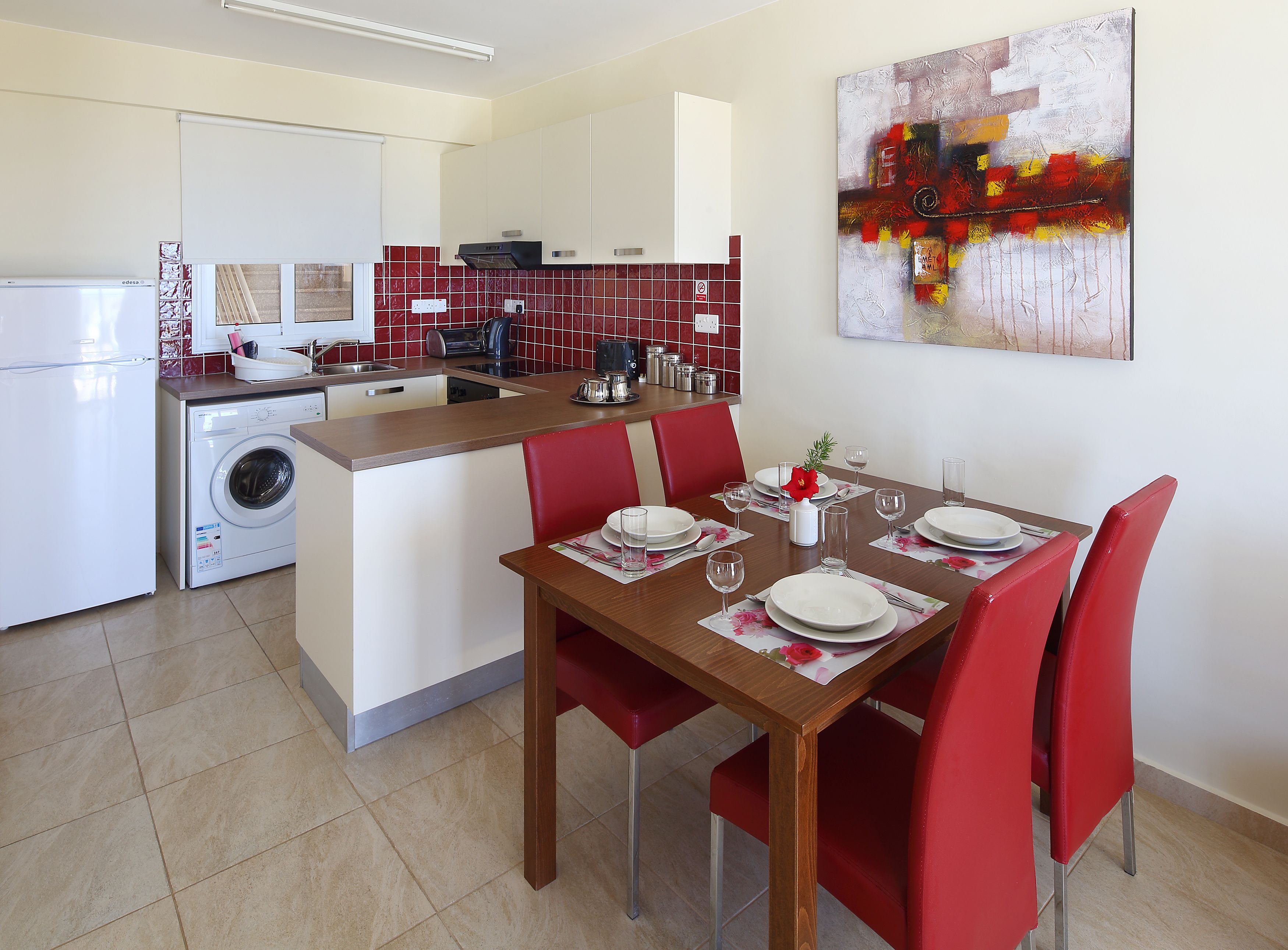 Una cocina moderna con comedor, lavadora y un salpicadero de azulejos rojos y blancos.