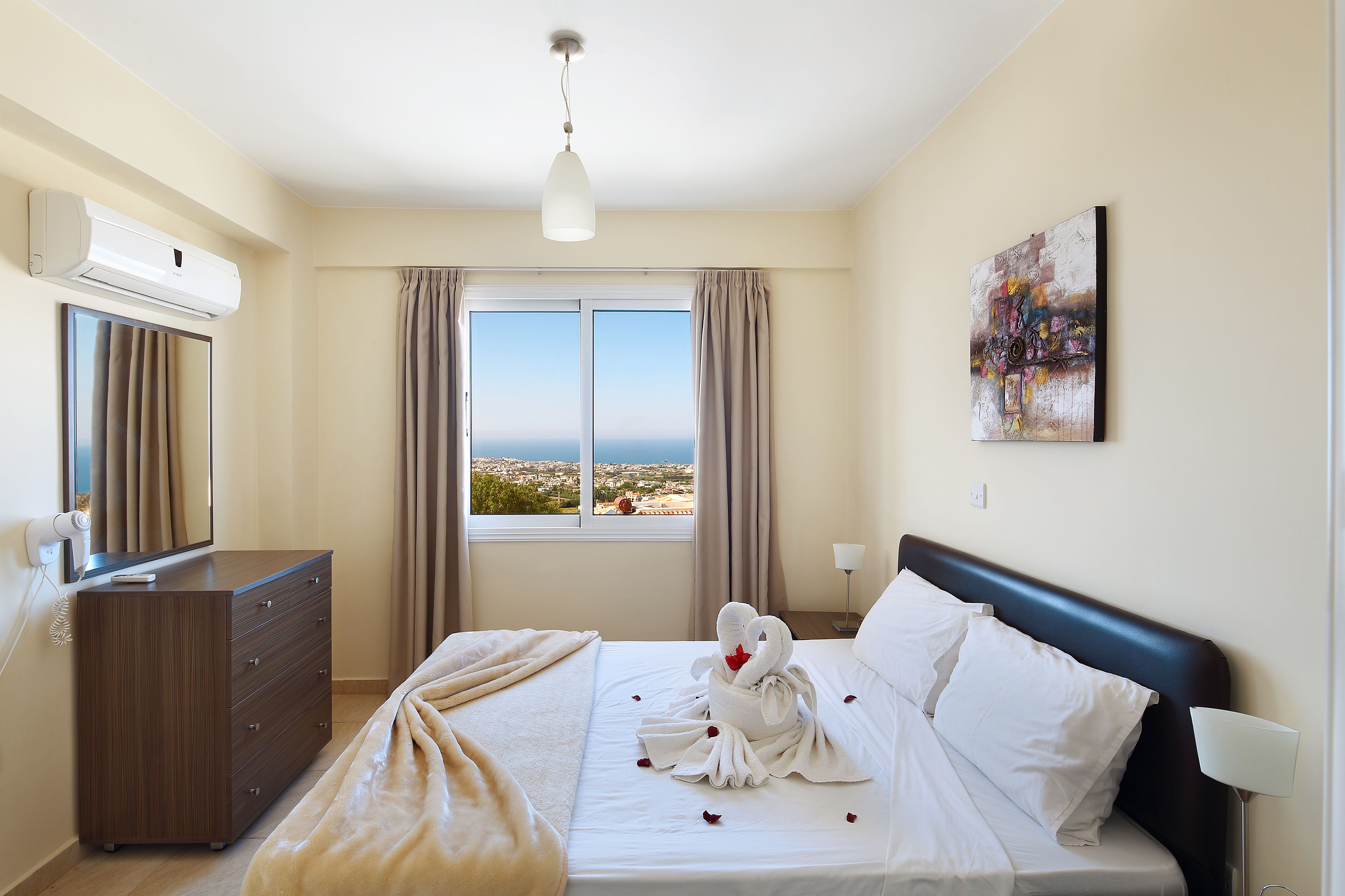 Una habitación de hotel con una cama, un tocador, una ventana con cortinas, un aire acondicionado de pared, un cuadro y una lámpara.